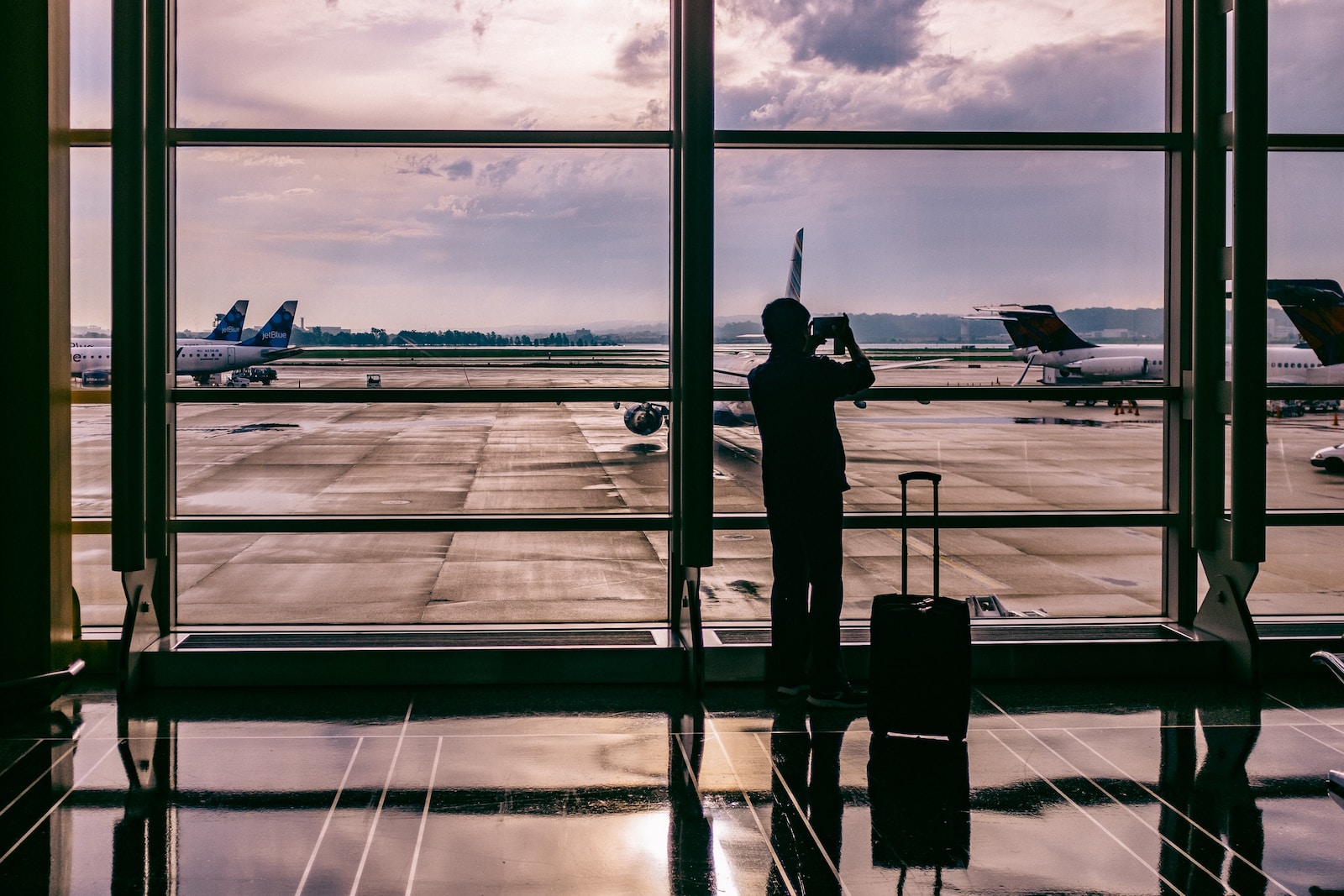 silhouette of person standing in front of glass while taking photo of plane